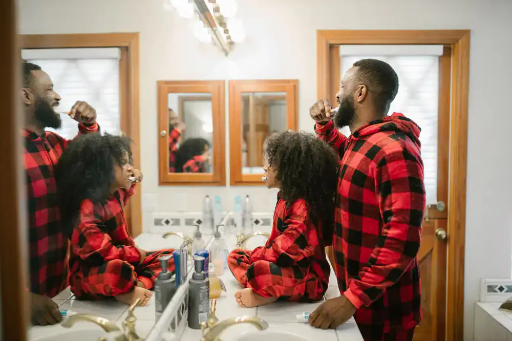 A parent assisting their smiling child with brushing teeth at home